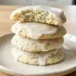 A stack of glazed lemon poppy seed cookies on a plate, with one cookie broken open to show the crumb.