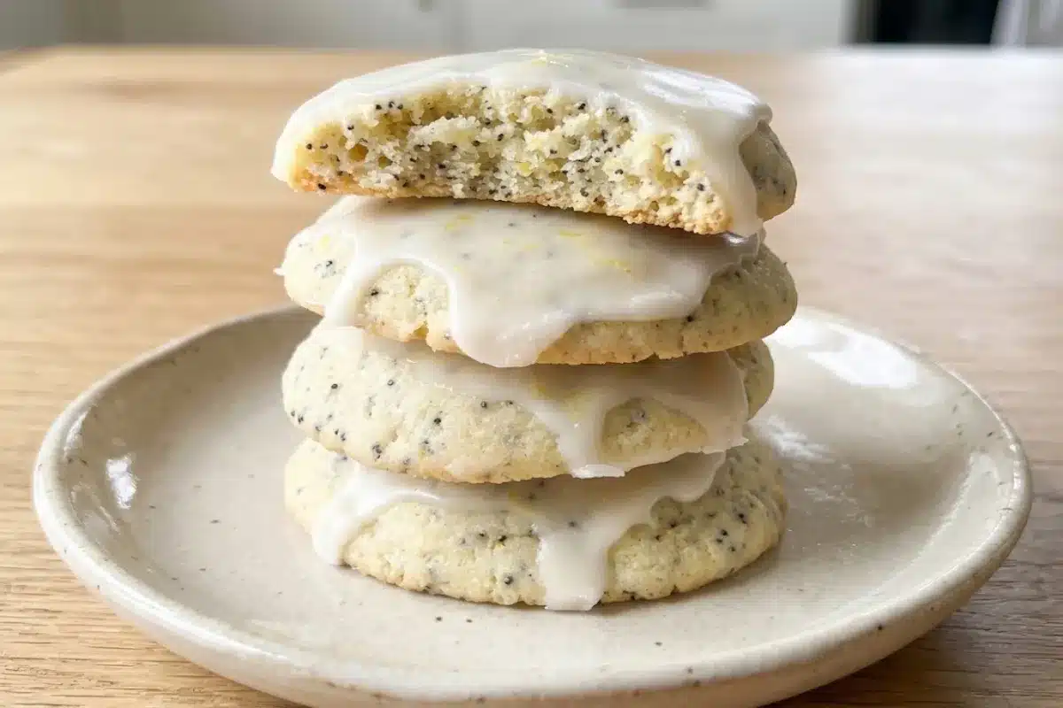 A stack of glazed lemon poppy seed cookies on a plate, with one cookie broken open to show the crumb.